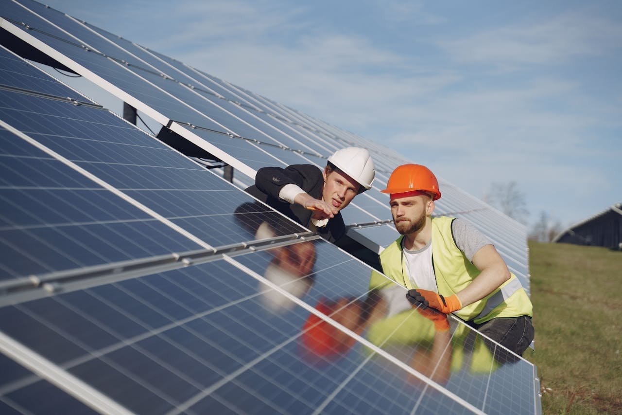 services-06 Concentrated male coworkers in hardhats working at solar energy station and discussing technical aspects of panels
